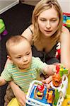Cute baby boy and his mother playing with the toys in playroom