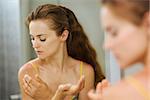 Young woman applying creme on shoulder in bathroom