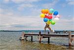 Boy holding balloons on wooden pier