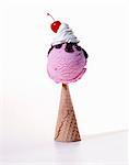 Scoop of Raspberry Ice Cream with Chocolate Sauce, Whipped Cream and a Cherry on an Upside Down Cone; White Background