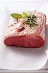 A piece of roast beef with herbs and garlic cloves