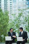 Business executives sitting outdoors with laptop computers, shaking hands