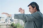 Mature businessman holding arms out in front of him and pointing, looking out of frame