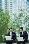 Business associates sitting outdoors with laptop computers