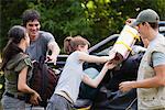 Young men helping young women loading camping gear onto back of pick-up truck