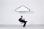 Businessman using laptop computer beneath cloud representing cloud computing