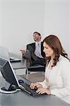 Geschäftsfrau, die im Büro arbeiten, während Kollege im Hintergrund lacht