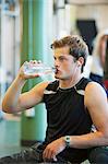 Young man drinking bottled water in gym room