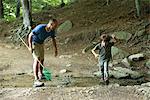 Father and son in woods, boy jumping over stream