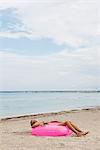 Girl lying on infltable ring on beach with eyes closed