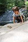 Boy crouching on rock looking at frog jump