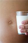 Pregnant woman holding glass of milk beside stomach, cropped