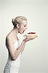 Jeune femme tenant un gâteau aux fraises avec la bouche ouverte, vue latérale, portrait