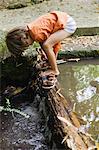 Boy putting on sandals by flowing water
