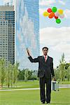 Businessman releasing bunch of balloons into air, looking disappointed