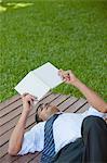 Man lying outdoors reading book