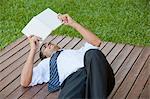 Mid-adult man lying outdoors reading book