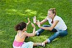 Mother and daughter sitting on grass playing patty-cake