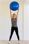 Mature woman holding fitness ball overhead with eyes closed