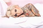 Porträt von nackte Frau mit Tattoo auf dem Bett liegend