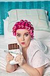 Portrait of shocked woman lying on bed with chocolate bar