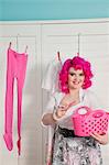 Portrait of a happy young woman with clothespin hanging clothes in room