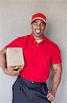 Portrait of a happy young man holding delivery box against wall