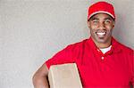 Portrait of a African American delivery man holding package against wall