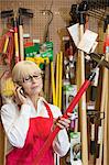 Senior female employee holding gardening tool while using mobile phone