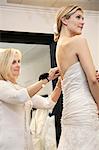 Beautiful woman dressed up in wedding dress while senior owner helping in bridal store