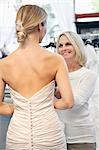 Back view of woman dressed in bridal gown with happy senior owner assisting