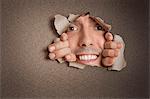 Portrait of a happy young Hispanic man peeking from ripped paper hole