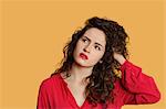 Thoughtful young woman with hand in hair over colored background