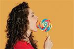 Side view of a young woman licking lollipop over colored background