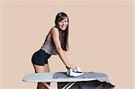 Portrait of a young woman ironing shirt over colored background