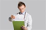 Male doctor reading medical records over gray background