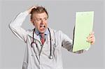 Male doctor terrified looking at medical reports over gray background