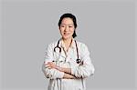 Portrait of an Asian female doctor standing with arms crossed over gray background