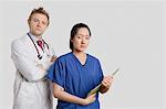 Portrait of a Caucasian doctor standing with an Asian nurse over gray background