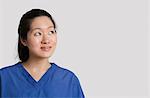 Young Asian female doctor looking up over gray background