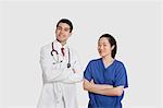 Portrait of male doctor and female nurse standing with hands folded over gray background