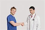 Porträt des Arztes und männliche Krankenschwester Händeschütteln auf grauem Hintergrund