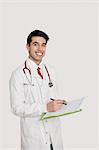 Portrait of a cheerful Indian male doctor holding a medical chart over light gray background