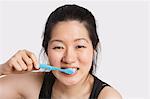 Portrait of a young woman brushing her teeth over light gray background