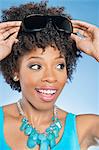 Cheerful African American woman adjusting sunglasses over colored background