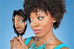 Close-up of African American woman looking at herself in mirror over colored background