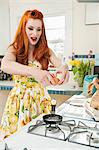 Young redheaded woman preparing omelet in kitchen