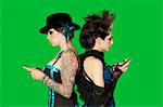 Side view of punk females standing back to back over with mobile phones over green background