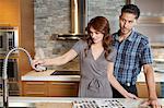 Young couple looking at sink faucet on kitchen counter in model home