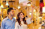 Young couple looking at price tag of lighting equipment in lights store